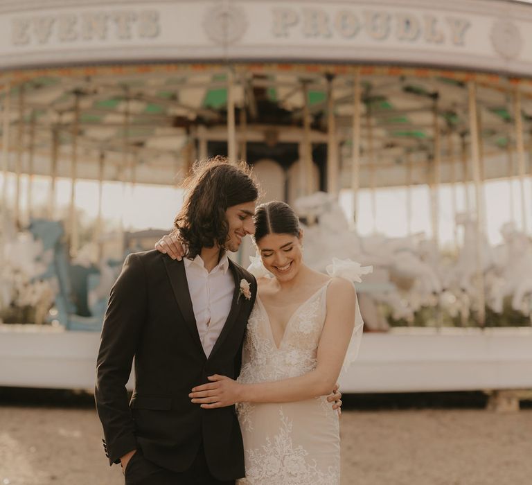 Stylish bride and groom posing in front of the carousel at Preston Court in a dinner suit and lace wedding dress 