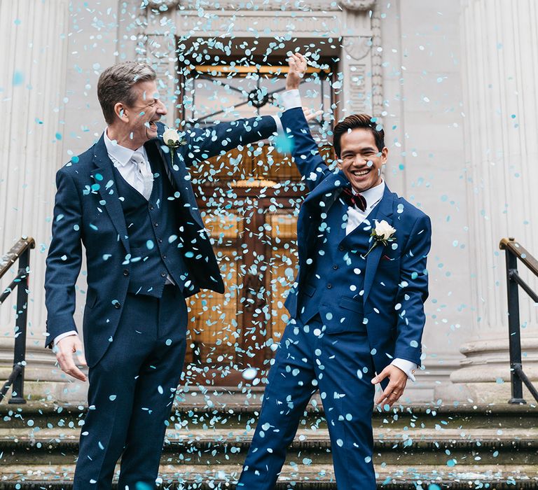 A gay couple hold hands lifted in the air during confetti shot after their wedding ceremony. Photography by Miss Gen. 