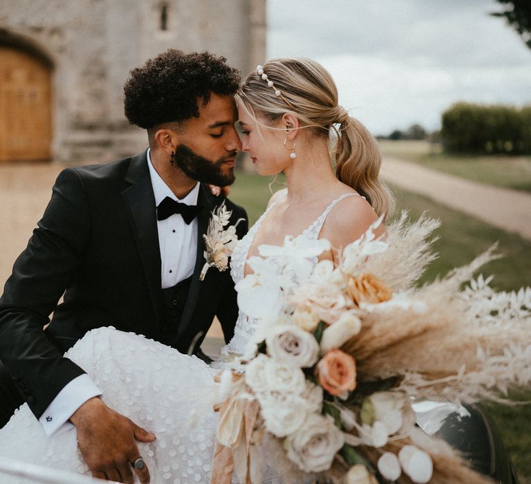 beaded groom in a three piece suit embracing his bride in a fitted wedding dress on the car bonnet 