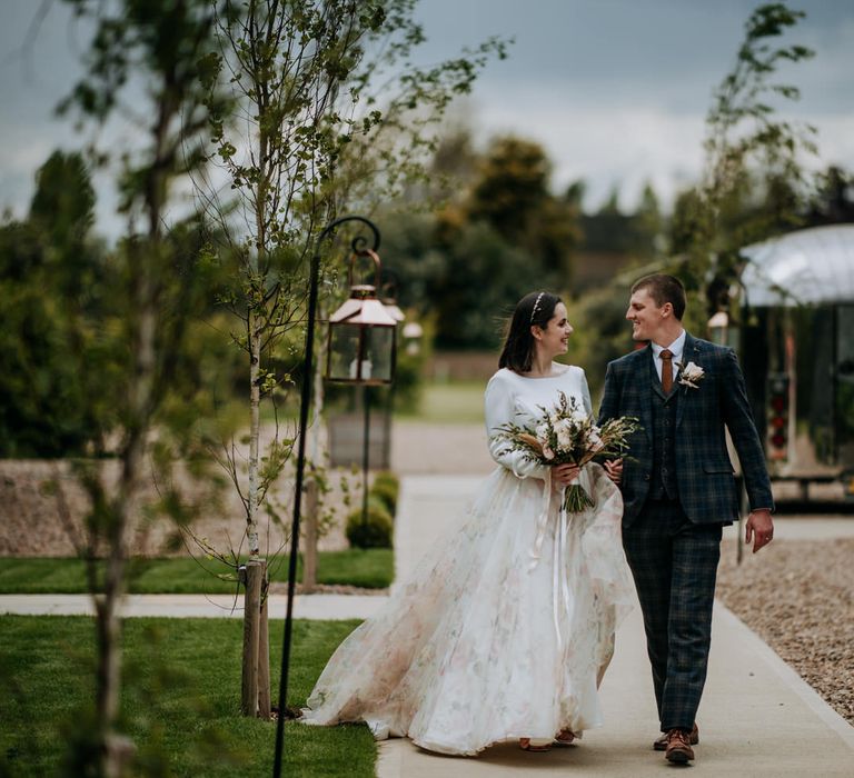 Bride and groom walking through the courtyard at East Yorkshire Barns in a navy and blue check suit and floral skirt wedding dress