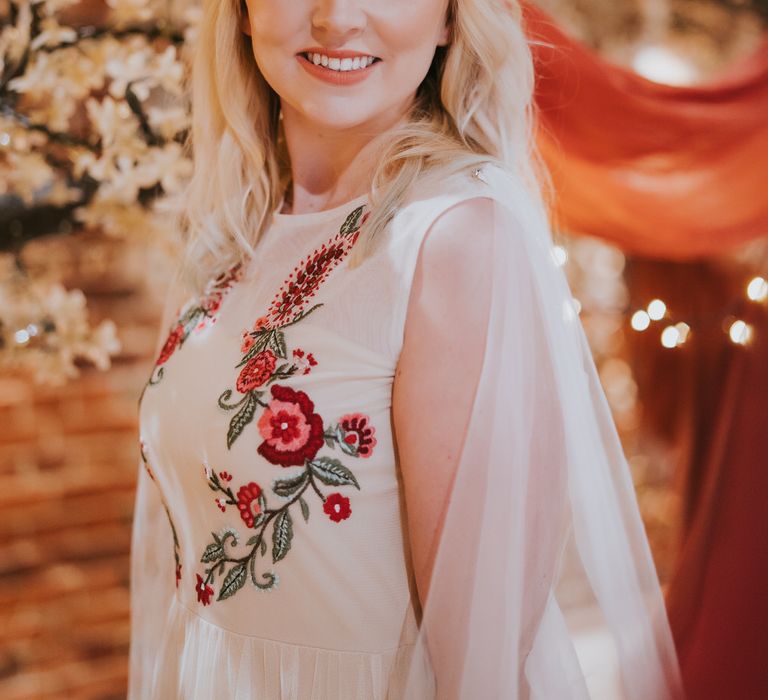 Blonde bride wearing a gold foliage hair accessory and sleeveless wedding dress with red flower embroidery