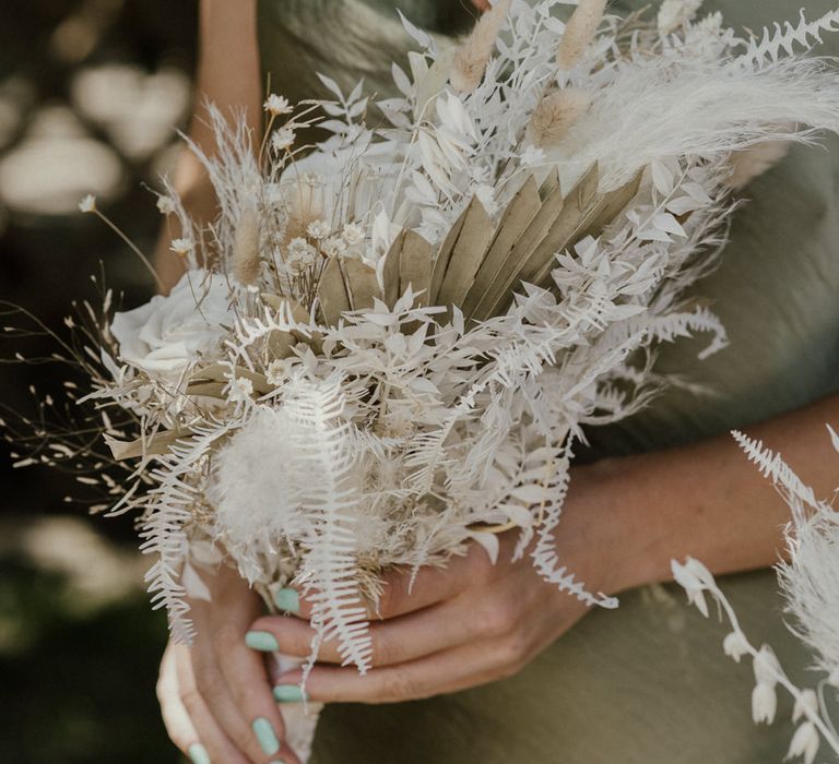 Bridesmaid in a sage green satin dress holding a dried flower bouquet with green nail polish