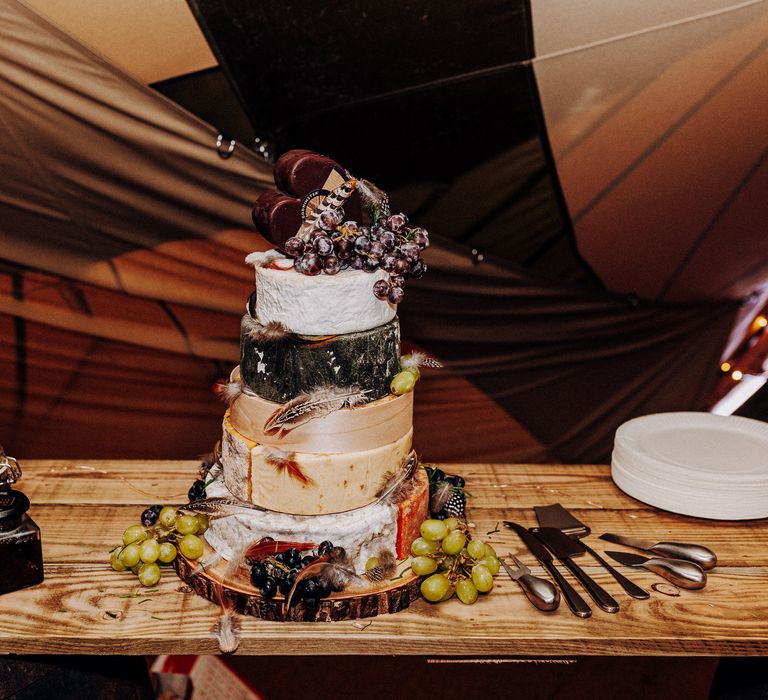 Cheese tower complete with feather decor set on wooden table with rustic vibe