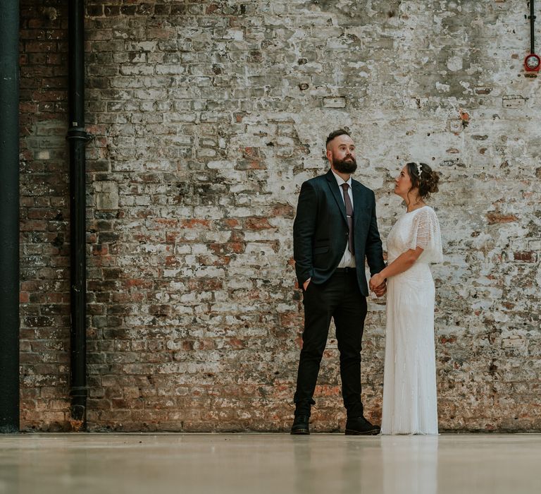 Bride & groom stand in front of industrial style brick wall for post-wedding ceremony photoshoot