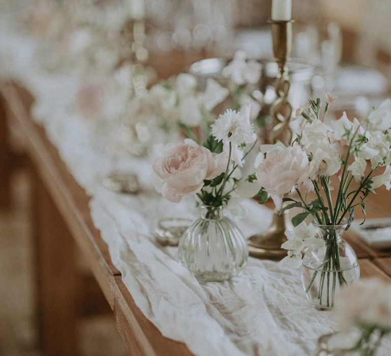 Pastel pink florals sit within small vases with green foliage for elegant reception table decor