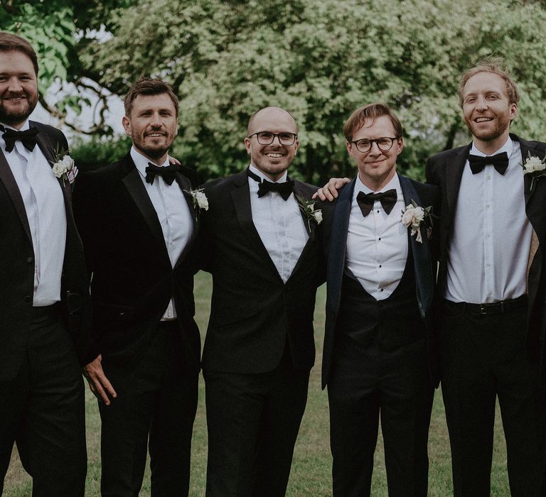 Groom stands with his groomsmen in black tie for classic wedding at Elmore Court