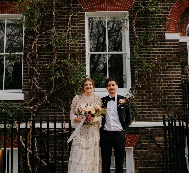 Bride & groom stand in front of town house covered in ivy on their wedding day