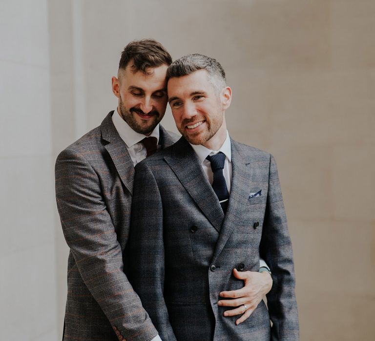 Grooms smile together as groom leans into his husband after wedding ceremony