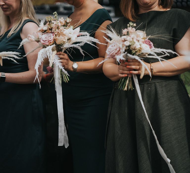 Bridesmaids wear deep green dresses whilst holding pampas grass bouquets on wedding day