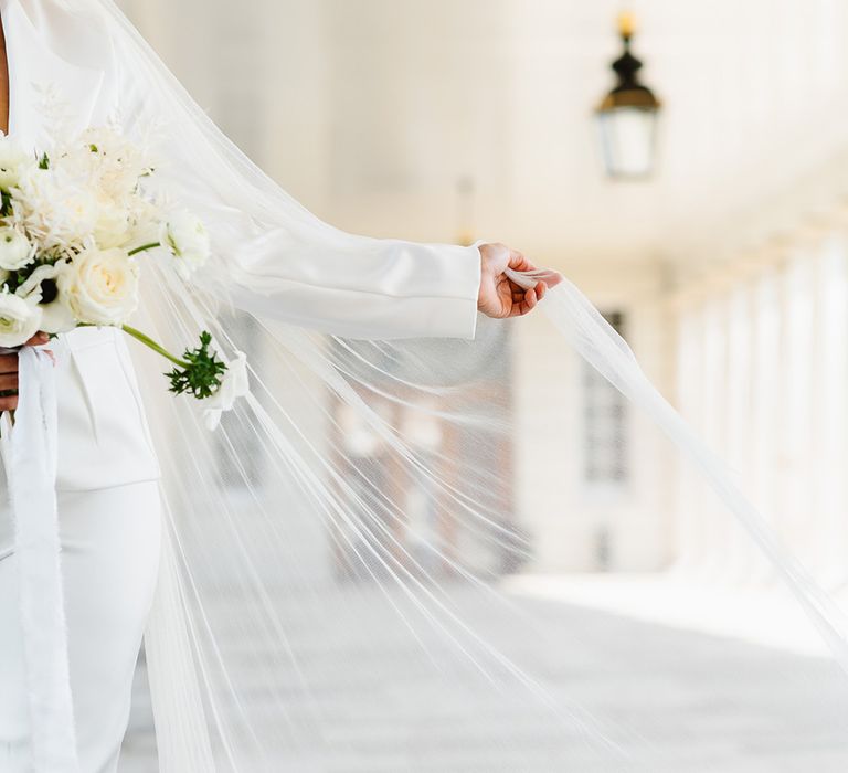 A bride holds her white veil out to the side.