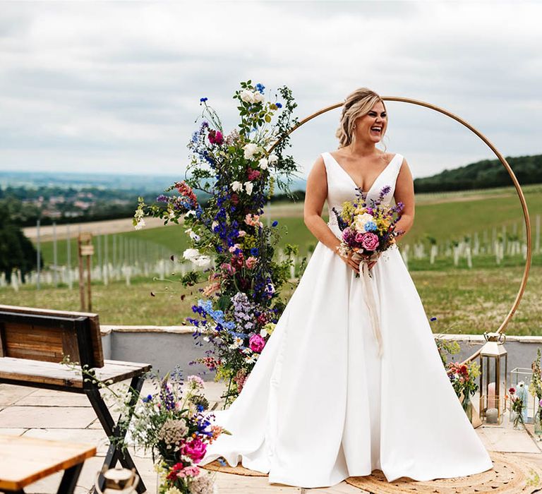 Bride in a princess wedding dress standing in front of a metal moon gate decorated with colourful wildflowers