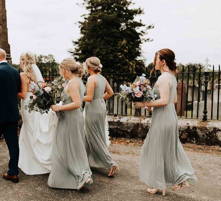 Sage green bridesmaids make their way into church with the bride