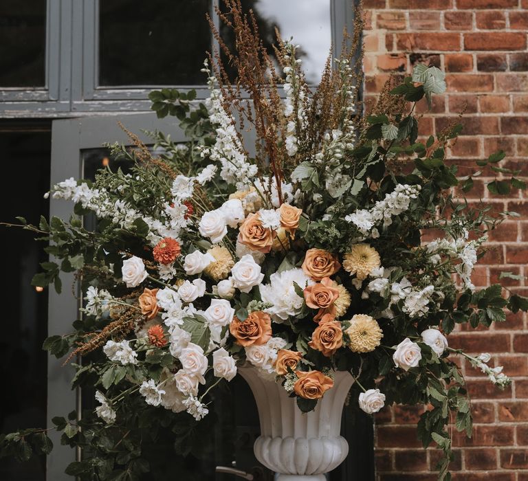 Large orange, yellow and white wedding floral arrangement in a white vessel 