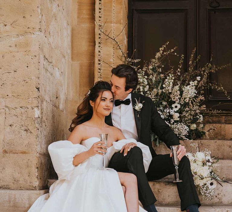 Groom in a tuxedo kissing his brides head on the steps at Bodleian Library 