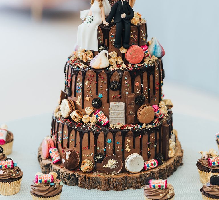 Chocolate drip wedding cake with macaroon, sweets and chocolate decor and iced people cake topper