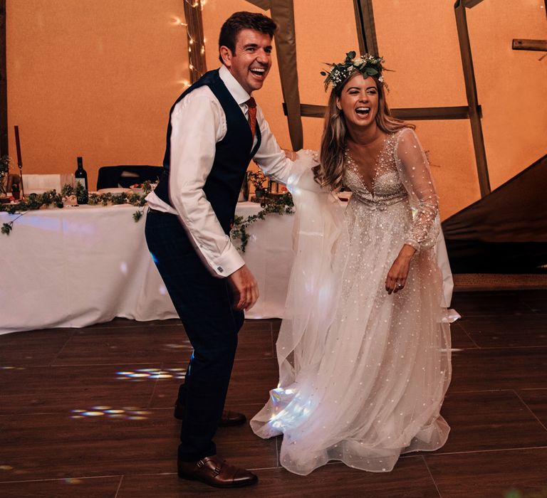 Bride in embroidered long sleeve wedding dress and flower crown dances with groom in waistcoat and red tie at tipi wedding reception