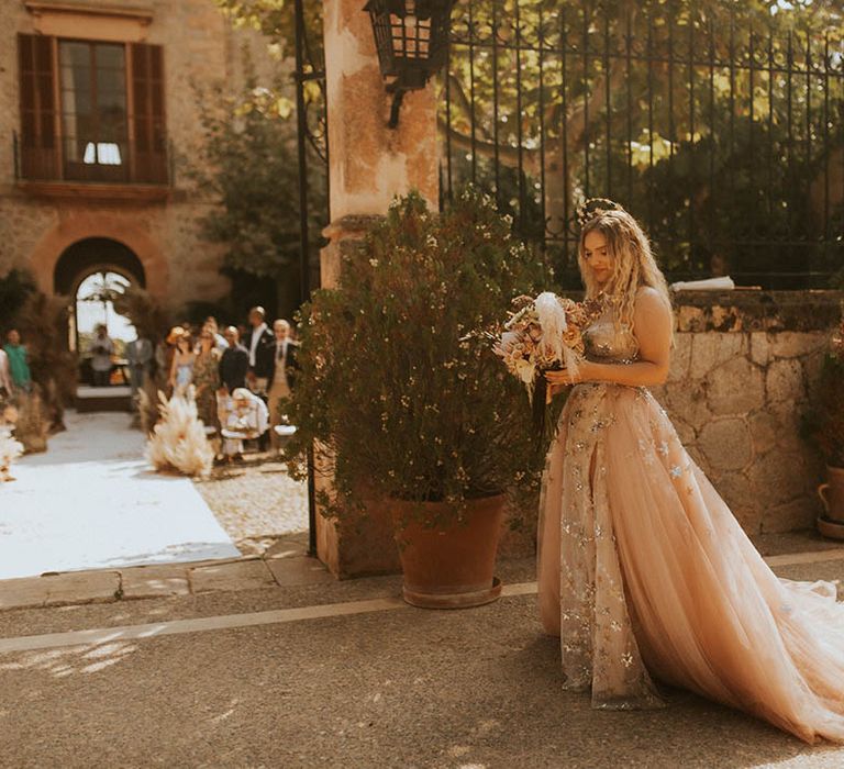 Bride walks to outdoor ceremony whilst holding bouquet 