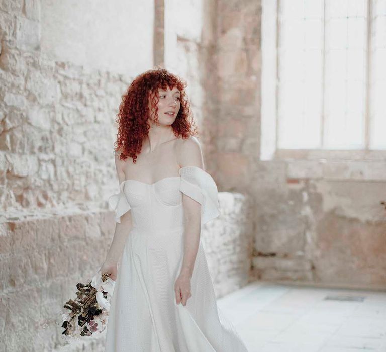 Bride with naturally curly red hair in a strapless wedding dress with Bardot sleeves and full skirt 