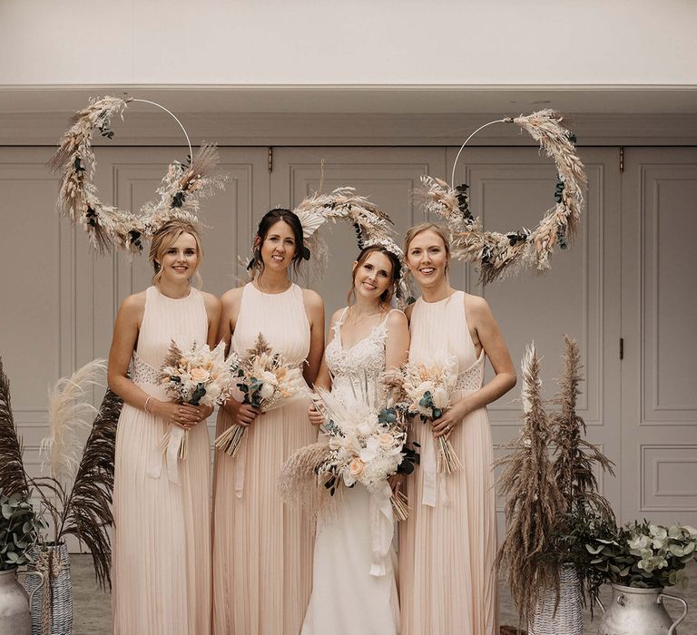 Bridesmaids stand with their bride in front of circular pampas grass installation 