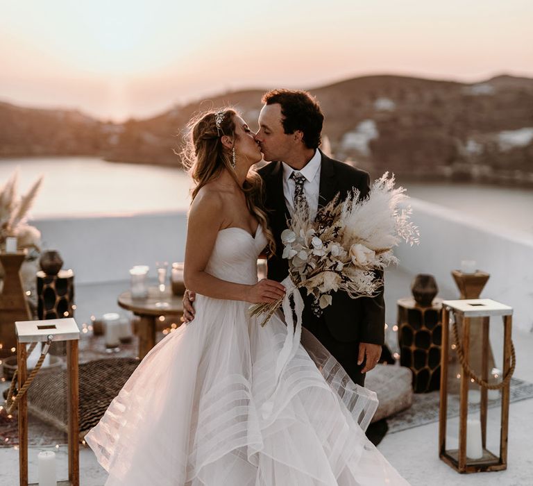 Bride & groom kiss outdoors in front of sunset on their wedding day