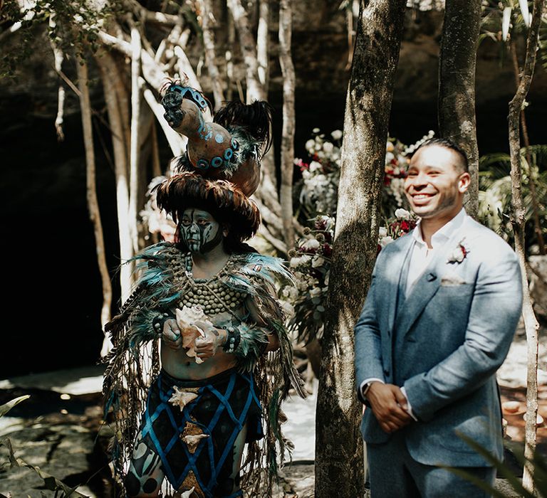 Groom in three-piece grey suit stands waiting for bride in traditional Mayan wedding ceremony 