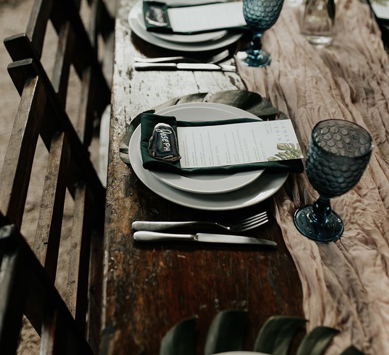 Blue coloured glassware with white plates, green napkins and leaf wedding stationery and Agate name tags