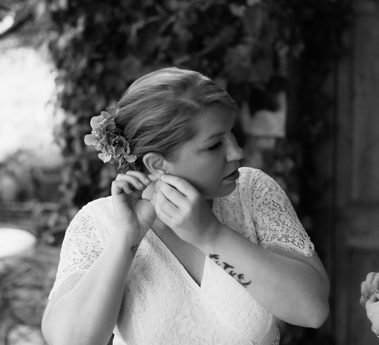 Bride in lace wedding jumpsuit with diamanté belt with blonde updo puts in her earrings