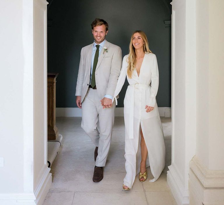 Bride in Bon Bride plunging neckline, long sleeved, front slit wedding dress with belt and Saint Laurent gold mules with groom in cream suit and green tie 