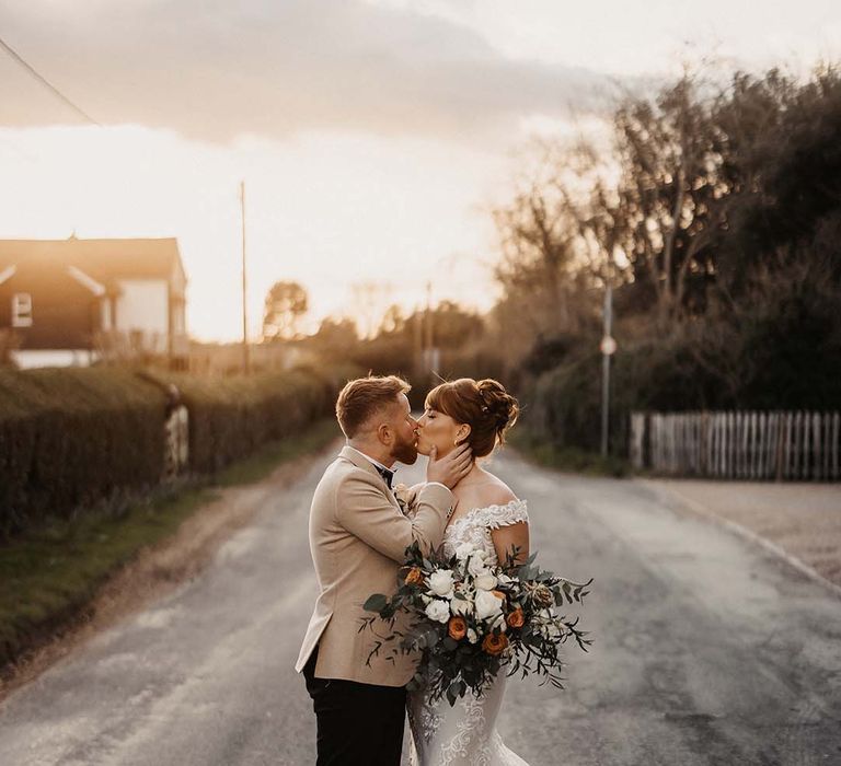 Bride and groom share a kiss for couple's portraits with white and orange wedding bouquet