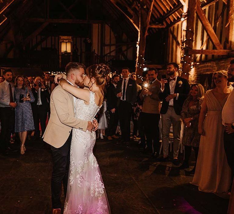 Bride and groom share their first dance in rustic Cooling Castle Barn wedding venue as the guests watch