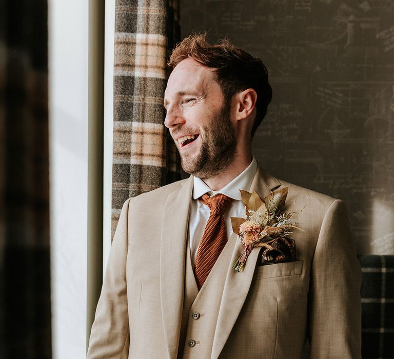 Groom in beige three piece suit with orange tie and dried flower boutonniere and patterned handkerchief 