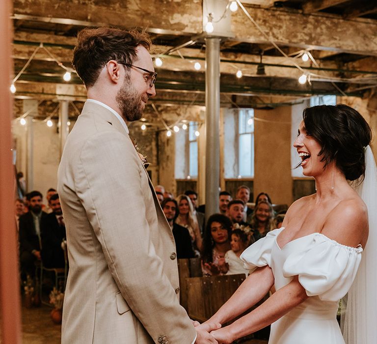 Bride in sweetheart puff sleeve Alexandra Grecco dress and groom in beige three piece suit 