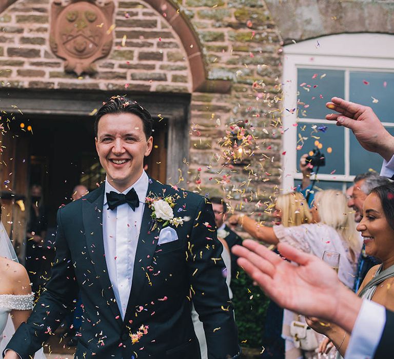 Groom in black tie and bride in sparkly off the shoulder Pronovias wedding dress have their colourful confetti exit