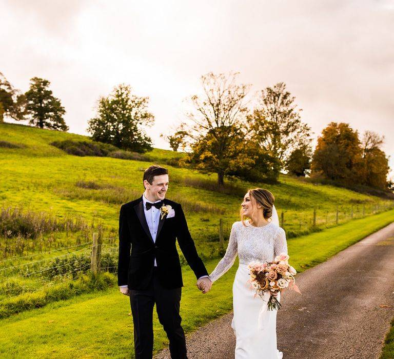 Bride and groom holding hands walking around their wedding venue together in black tie