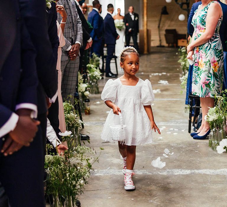 Flower girl in short puff sleeve white dress, pink converse and pearl headband walks down the aisle