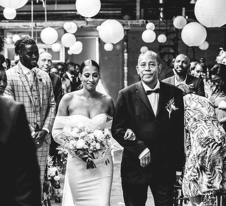 Father of the bride in black tie walks the bride down the aisle in off the shoulder sheer sleeve wedding dress 