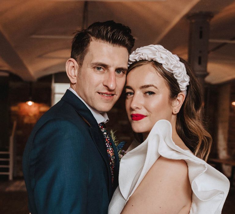 Groom in blue suit and floral tie holds onto the bride tightly wearing Jesus Peiro wedding dress with statement sleeves and ruffle headband 