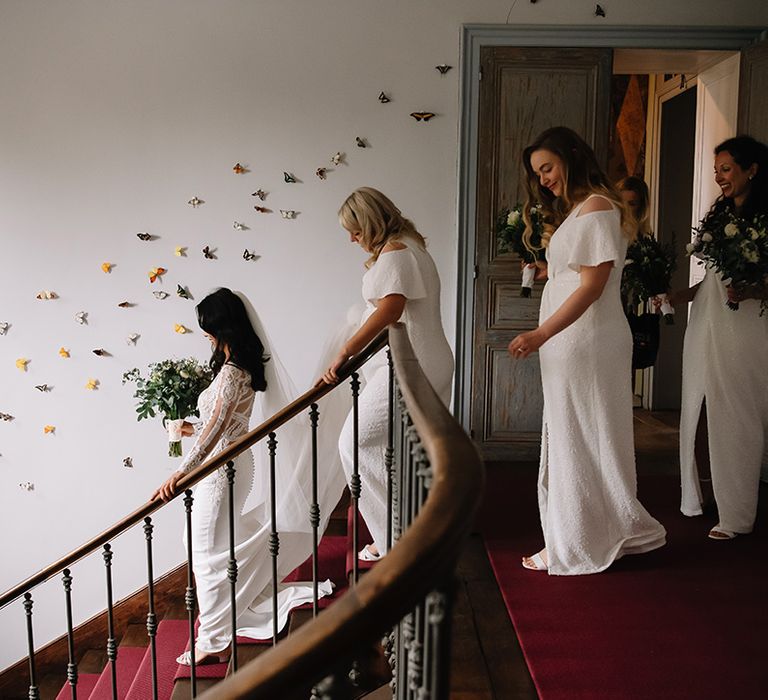 Bridesmaids in white sparkly front slit dresses follows the bride down the stairs to travel to the wedding ceremony 