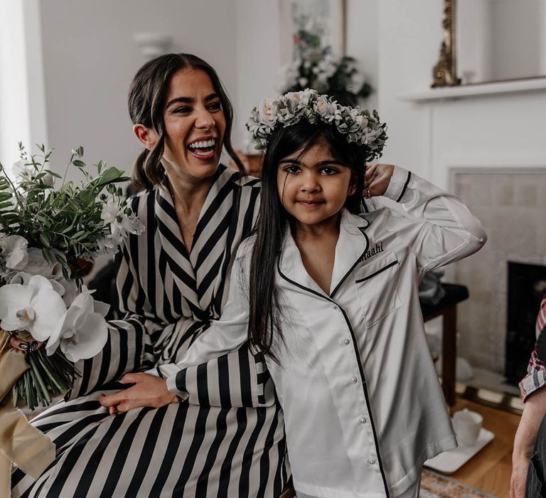 Bride in black and white stripy pyjamas on the wedding morning with the flower girl in white satin PJs and a flower crown 