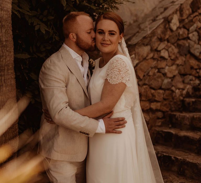 Bride & groom stand outdoors in front of rustic backdrop in Spain 