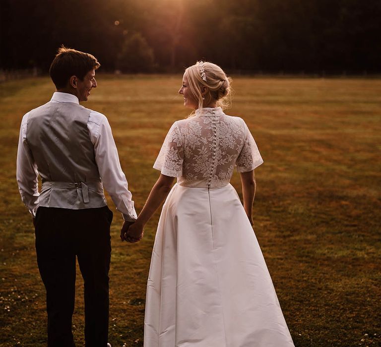 Bride in lace button back Jesus Peiro wedding dress with a white headband accessory with the groom in a grey waistcoat and striped trousers 