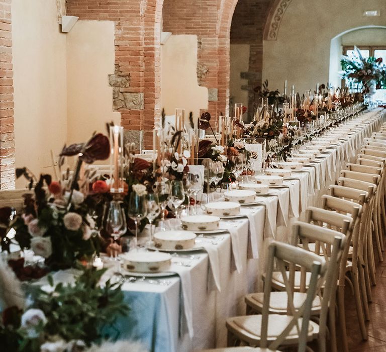 Banquet table complete with white table cloth, tambourine wedding favours, pillar candles and Autumnal coloured bouquets lining the middle of the table