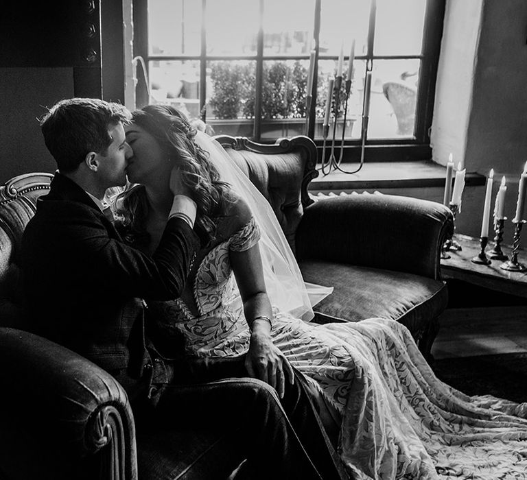 Bride and groom share an intimate kiss as they sit on a sofa together 