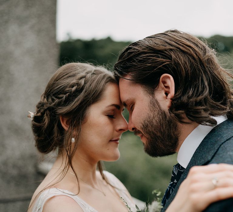 Bride wears her brown hair in low curled bun finished with plaits either side 