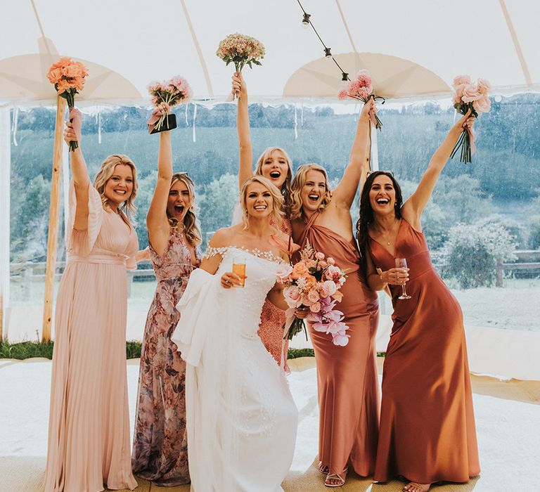 Bridesmaids in mismatched pink bridesmaid dresses with bride in an off the shoulder wedding dress in the marquee 