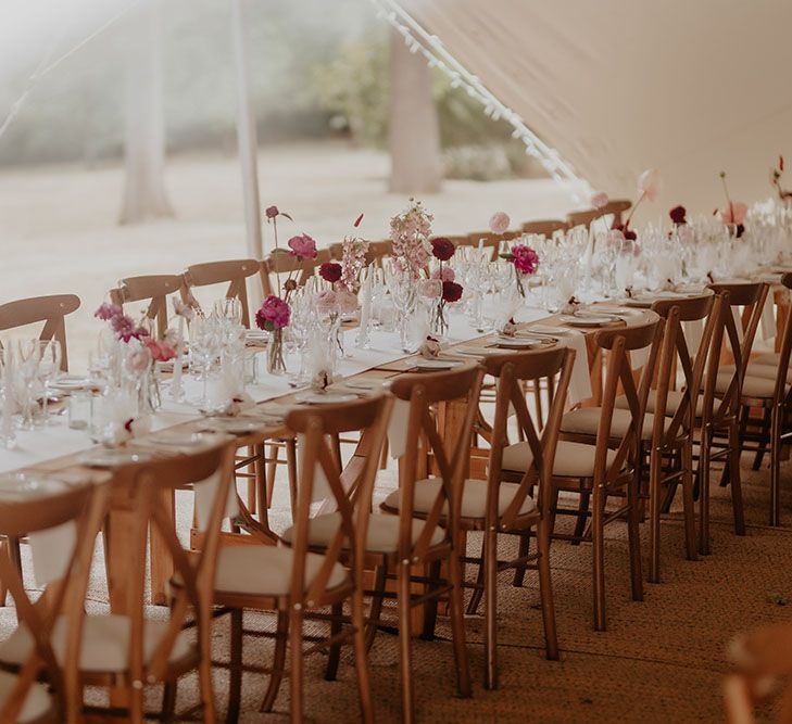 Wooden banquet tables with white tablecloth runner and white and pink floral arrangements lining the middle 