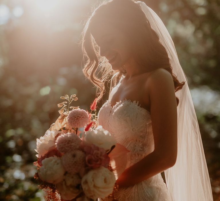 Bride stands in the sunshine as it begins to set during golden hour and golds bridal bouquet whilst wearing fitted Pronovias wedding dress