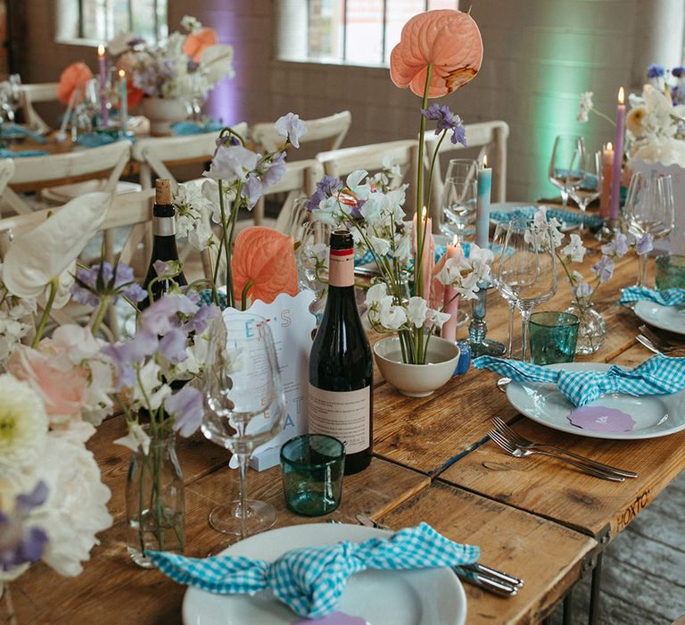 Pastel coloured wedding table setting with blue and white gingham napkin, pastel candles and flowers and purple place names