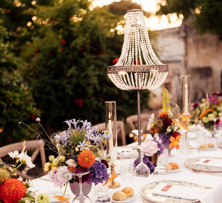 Outdoor destination wedding tablescape for Italian wedding with chandelier installations, colourful flower arrangements and speckled plates