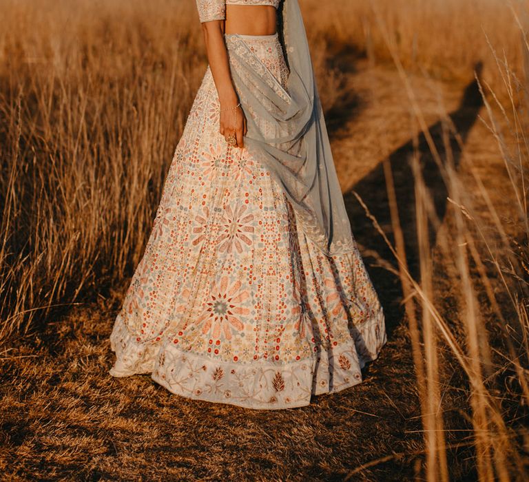 Beautiful Indian bride wears colourful pastel lehenga with statement necklace and her hair tied back into intricate plait style 